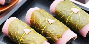 Sakura-Mochi auf schwarzem Tablett serviert mit Teegeschirr im Hintergrund