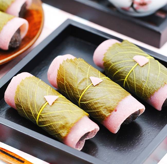 Sakura-Mochi auf schwarzem Tablett serviert mit Teegeschirr im Hintergrund