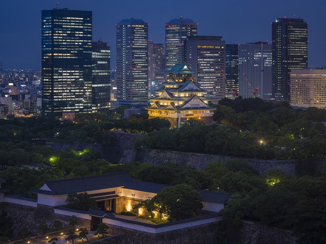 Die stattliche Burg Osaka angeleuchtet vor den nächtlichen Hochäusern