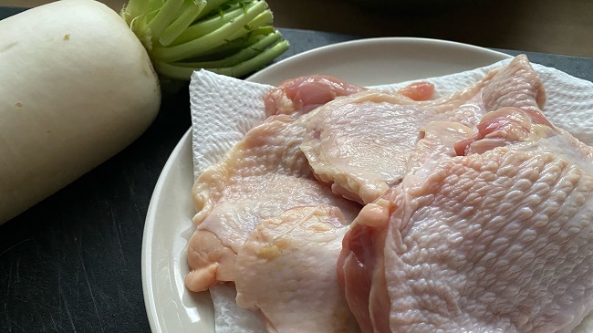 Rohes Hähnchenfleisch auf Teller neben ungeschältem Rettich