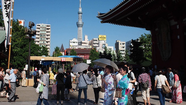 Besucher:innen spazieren über das Tempelgelände, im Hintergrund ragt der Tokyo Sky Tree auf