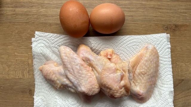Rohe Hähnchenflügel auf einem Küchentuch, daneben zwei ungeschälte gekochte Eier