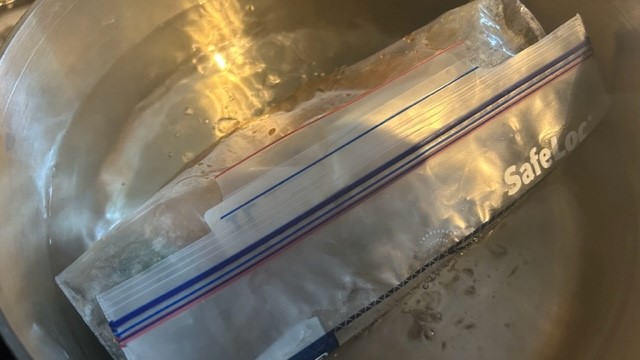 Plastikbeutel mit Hähnchenbrust in Marinade liegt im heißen Wasser