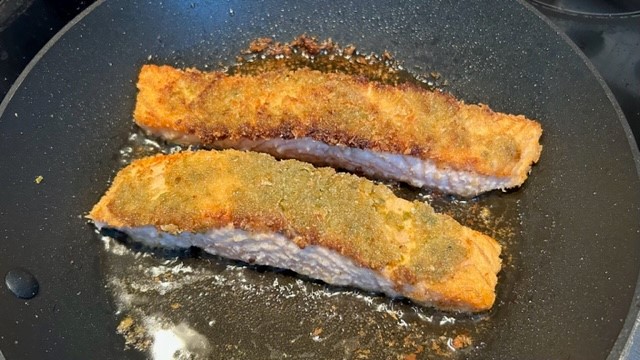 Paniertes Lachsfilet wird in der Pfanne gebraten