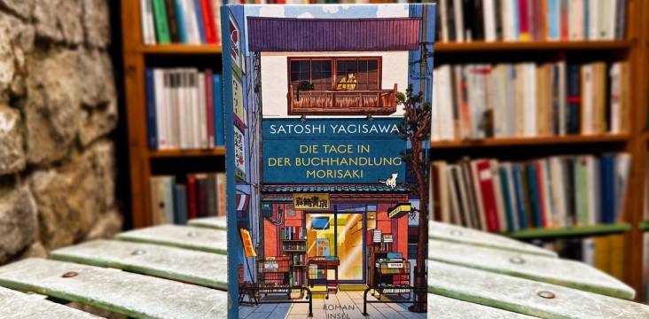 Roman "Die Tage in der Buchhandlung Morisaki" mit einem Bücherregal im Hintergrund