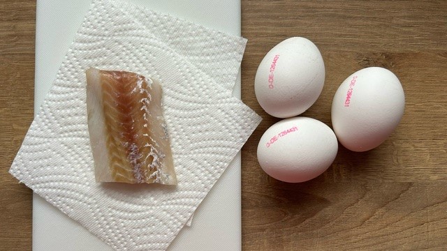 Weißfisch auf Küchenpapier und drei rohe Eier