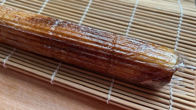 In Frischhaltefolie eingepackte, abgekühlte Teigrolle auf Bambusmatte