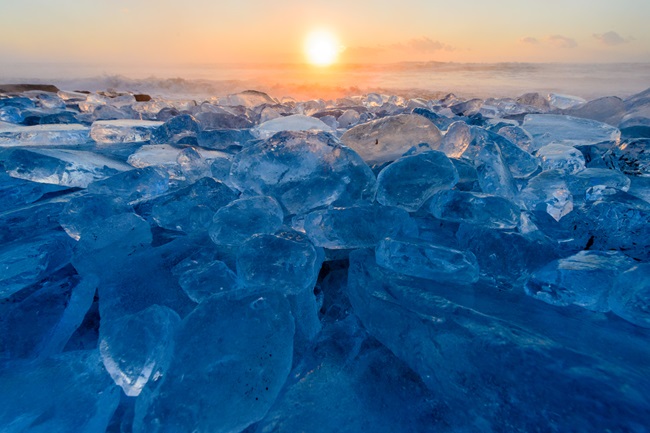 Jede Menge angespültes Eis türmt sich am Strand auf und glitzert bläulich vor der aufgehenden Sonne