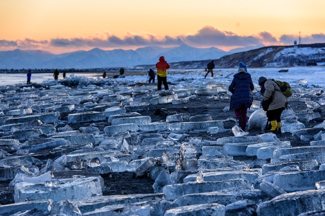 Mit Eis bedeckter Strand im Abendlicht, vereinzelte Besucher