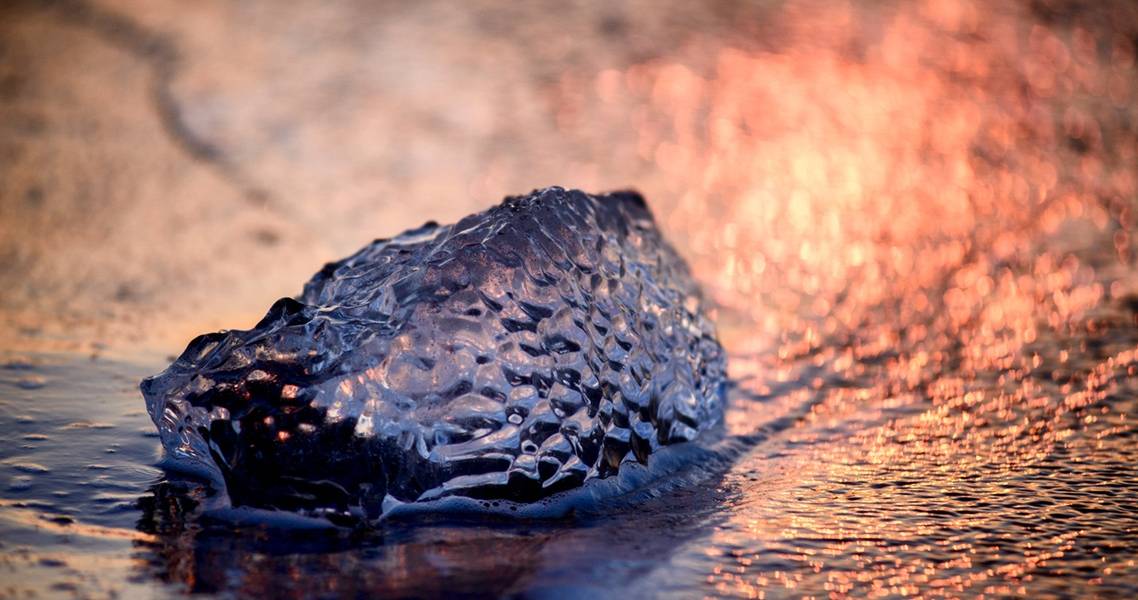 Im rosafarbenen Abendlicht glitzernder Eisblock im Meer