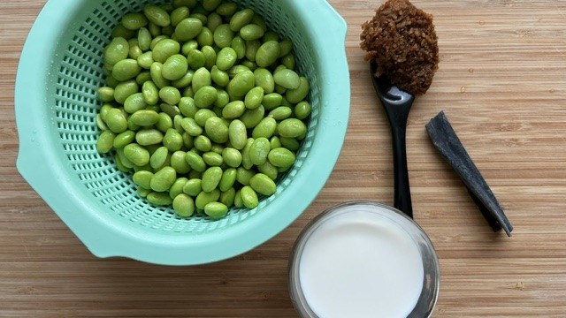 Edamame im Sieb, Miso-Paste auf Löffel, ein Glas Sojamilch und Kombu