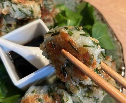 Daikon-Mochi wird mit Holzstäbchen über einen Teller mit Sauce, Salat und weiteren Mochi gehalten