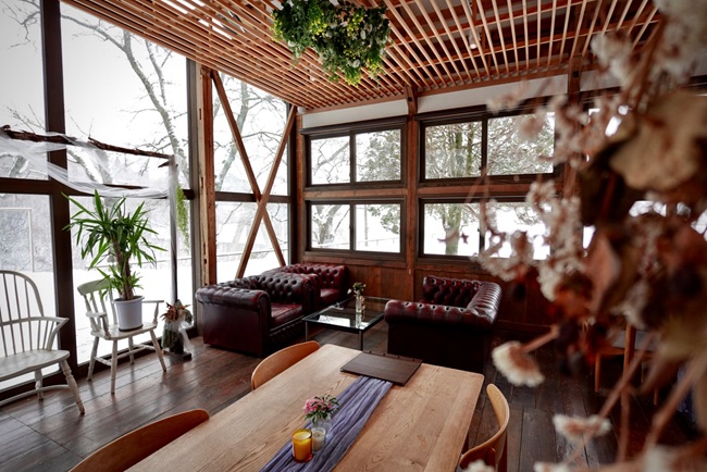 Innenraum des yodge (Café) mit Sesseln, langem Tisch und Blick in die verschneite Landschaft.