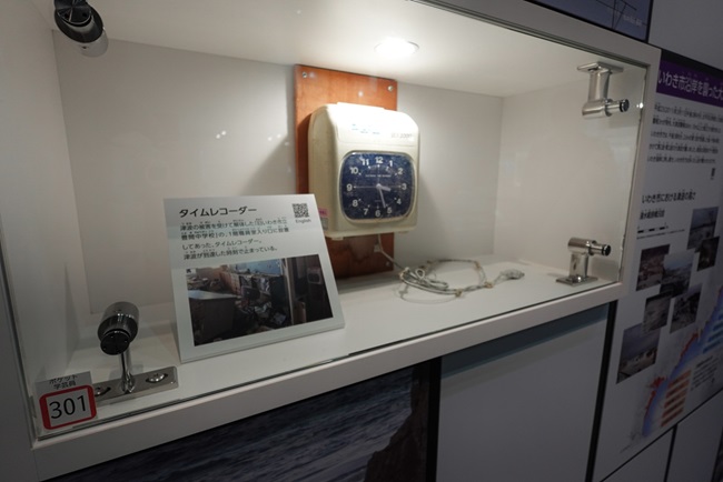 Schaukasten im Iwaki 3.11 Memorial and Revitalization Museum, der eine Stechuhr zeigt, die zum Zeitpunkt des Tsunamis stehenblieb.