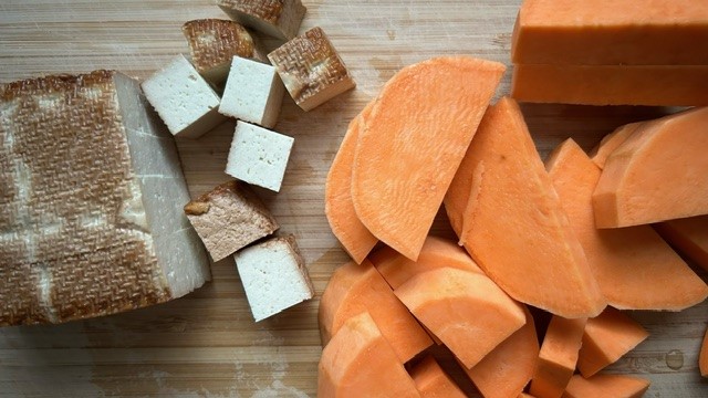 Tofu (teil in Würfel geschnitten) und Süßkartoffel in Viertel geschnitten auf einem Holzbrett