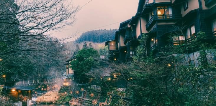 Kurokawa Onsen im Winter: Das warme Licht der Bambuslaternen spiegelt sich auf dem Wasser, am Horizont sind Berge zu sehen