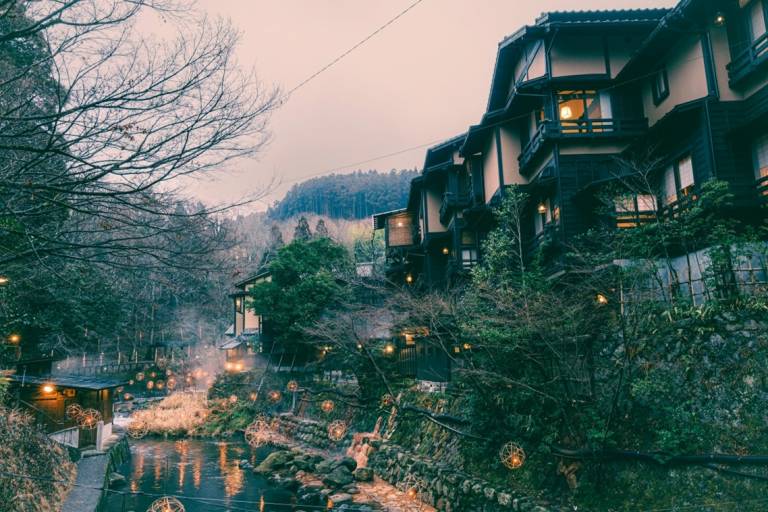 Kurokawa Onsen im Winter: Das warme Licht der Bambuslaternen spiegelt sich auf dem Wasser, am Horizont sind Berge zu sehen