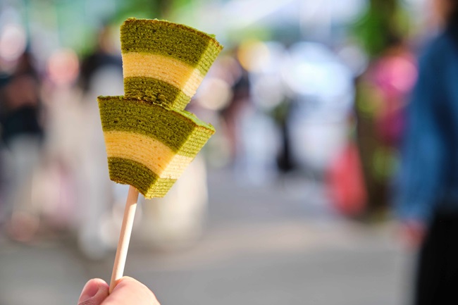 Eine Hand hält zwei Baumküchenstücke am Spieß mit Matcha-Geschmack