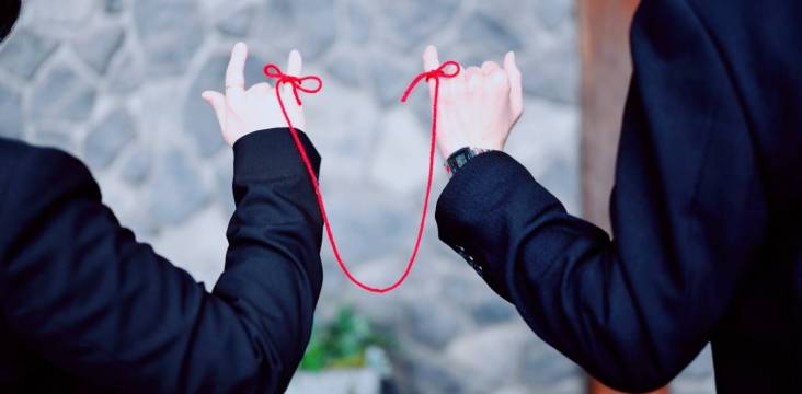 Zwei Menschen sind mit einem roten Faden um ihre kleinen Finger miteinander verbunden